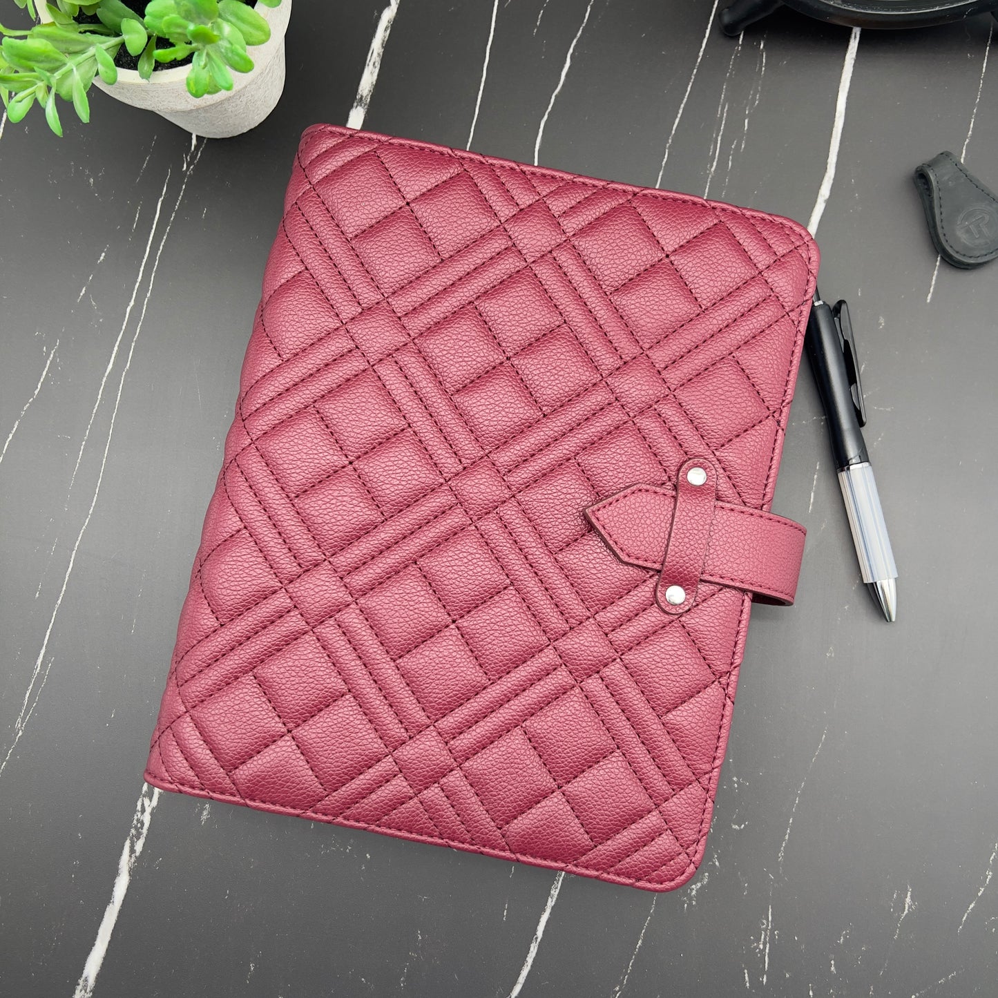 Pink quilted planner cover on a gray surface with a pen and plant.