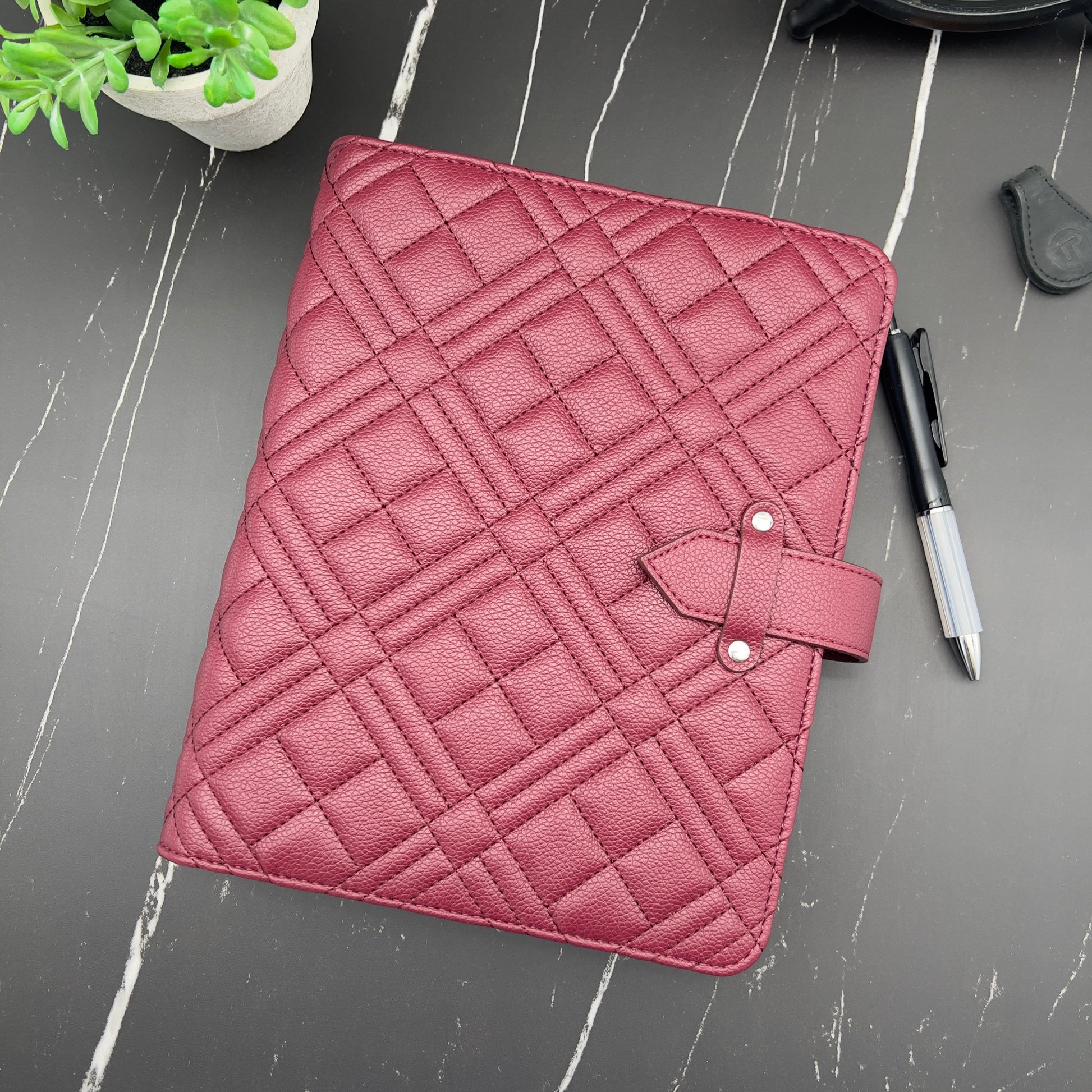 Pink quilted planner cover on a gray surface with a pen and plant.