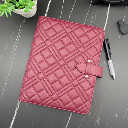 Pink quilted planner cover on a gray surface with a pen and plant.