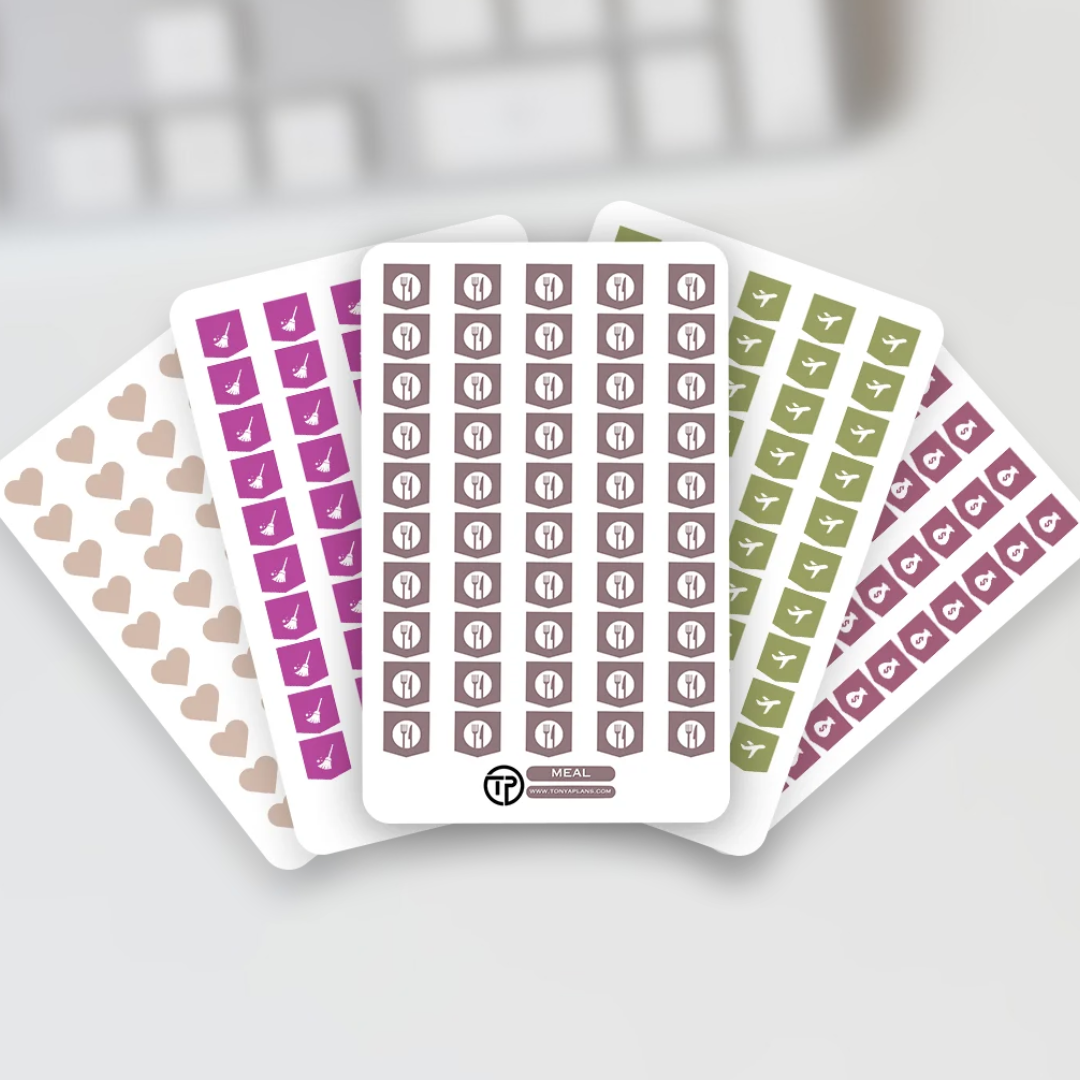 Four sheets of planner stickers fanned out on a light gray surface. The sheets include beige hearts, purple checkmarks, brown calendar-day squares, and green calendar-day squares, with a blurred keyboard in the background.