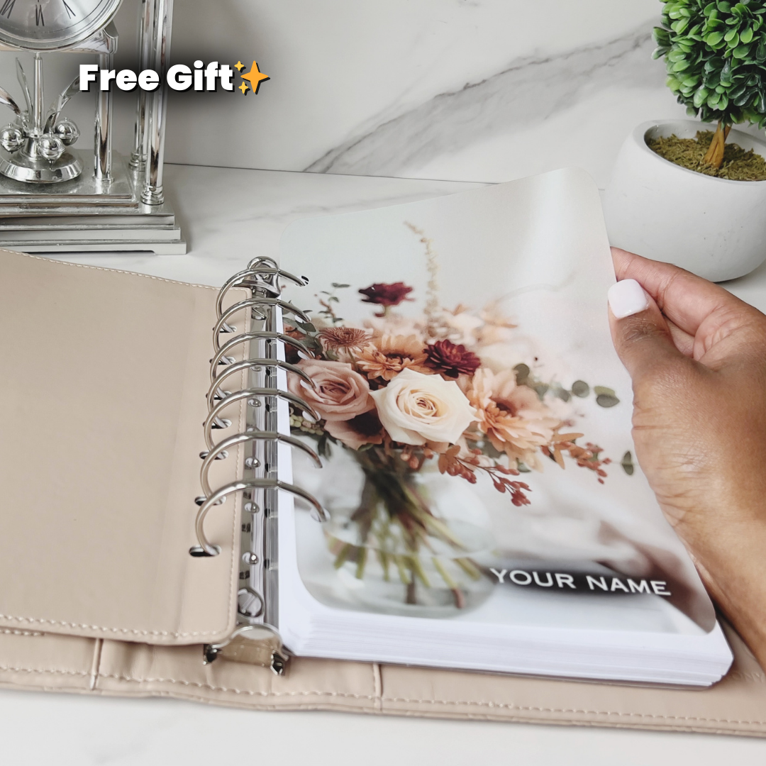 Person holding a planner with a floral design and 'Your Name' text on a marble surface.