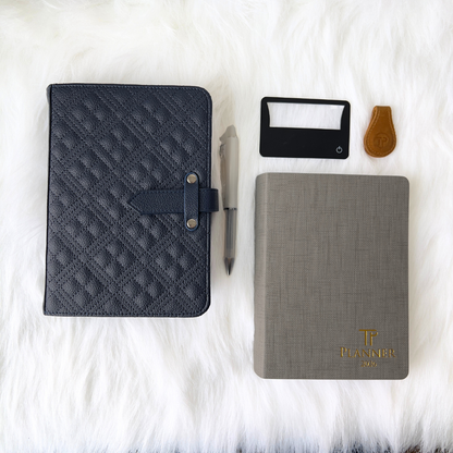 Quilted dark gray notebook, gray notebook with gold logo, pen, card, and keychain on a white surface.
