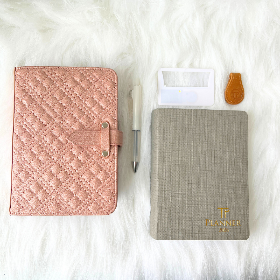 Pink quilted planner, gray planner with 'TP Planner' logo, pen, and clear case on a white fur background