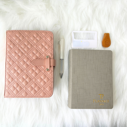 Pink quilted planner, gray planner with 'TP Planner' logo, pen, and clear case on a white fur background